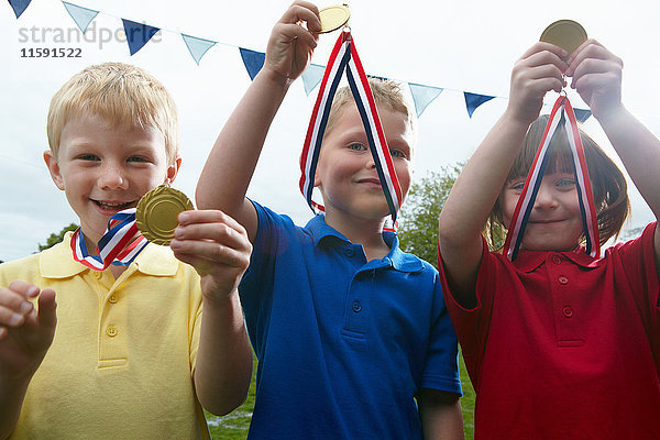 Drei Kinder mit Sportmedaillen auf dem Schulhof