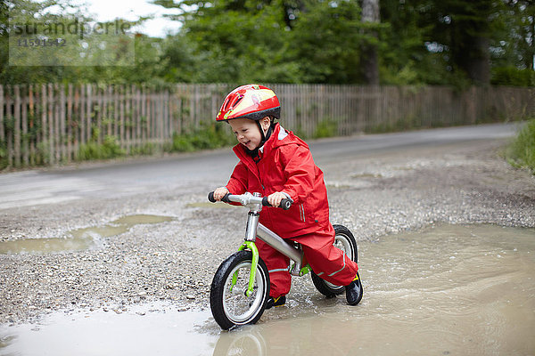 Lächelnder Junge fährt Fahrrad in Pfützen