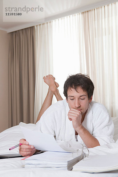 Mann im Bademantel macht Papierkram im Bett