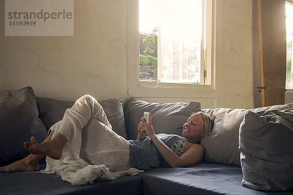 Lächelnde Frau auf der Couch liegend mit dem Handy