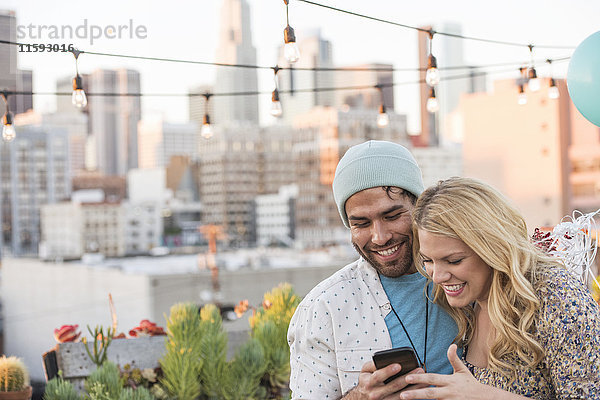 Junges Paar mit Luftballons auf der Dachterrasse mit Smartphone