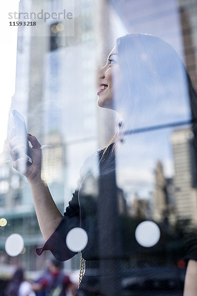 USA  New York City  Manhattan  lächelnde junge Frau hinter Glasscheibe  die etwas schaut