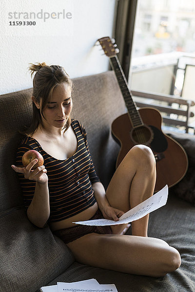 Junge Frau mit Noten und Gitarre auf der Couch sitzend