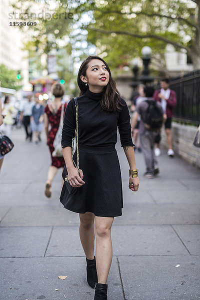 USA  New York City  Manhattan  modische junge Frau in schwarz gekleidet  auf dem Bürgersteig laufend
