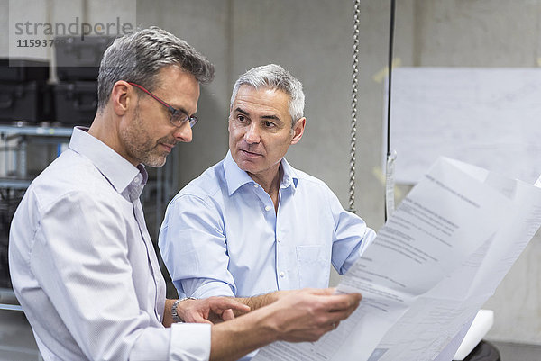 Zwei Geschäftsleute in der Fabrikhalle diskutieren den Bauplan