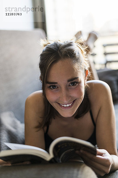 Lächelnde junge Frau in Dessous Lesebuch auf Couch