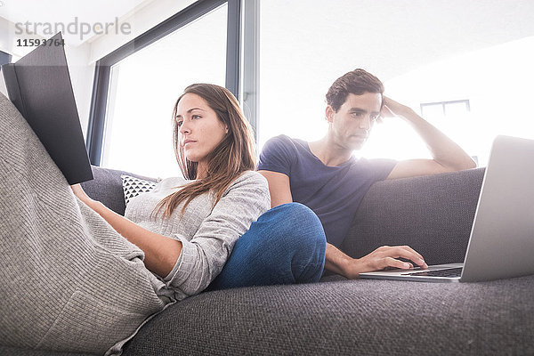 Junges Paar auf der Couch entspannt mit Buch und Laptop