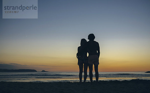 Junges Paar beobachtet den Sonnenuntergang am Strand
