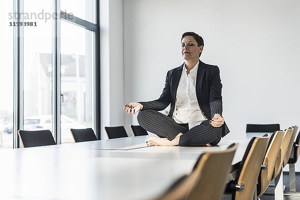 Geschäftsfrau auf dem Konferenztisch sitzend meditierend