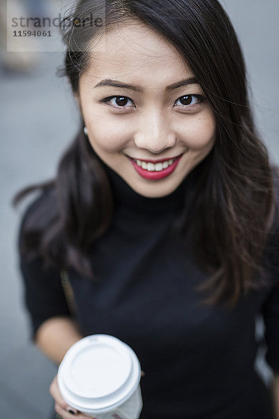 Porträt einer lächelnden jungen Frau mit Kaffee zum Mitnehmen