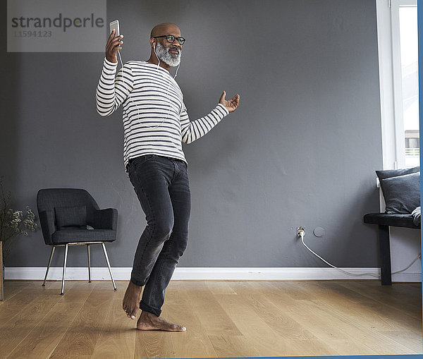 Ein reifer Mann  der alleine zu Hause tanzt und ein Smartphone hält.