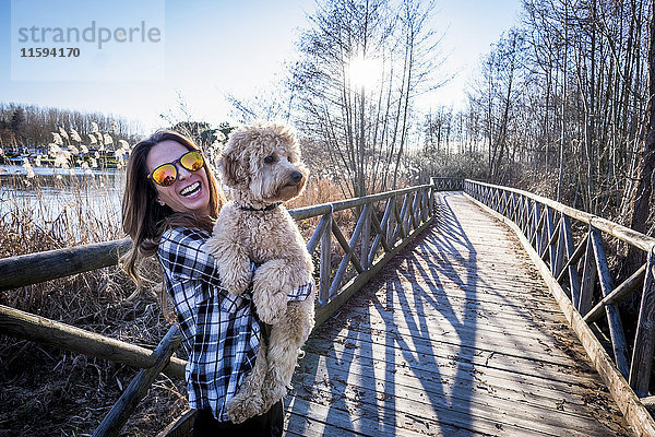 Frau steht auf der Brücke und hält ihren Hund.