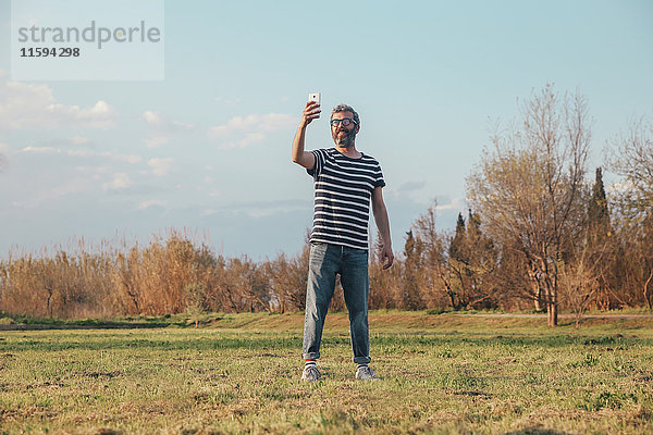 Mann steht auf einer Wiese und fotografiert mit dem Smartphone