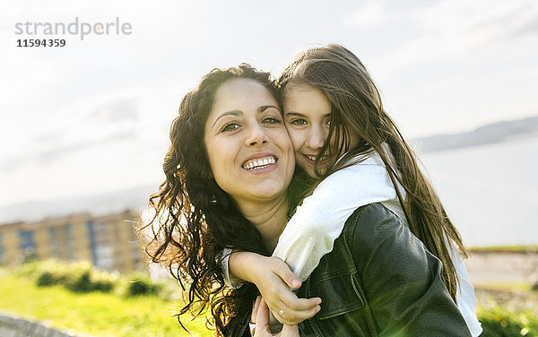 Porträt einer glücklichen Mutter  die eine Tochter im Freien trägt.