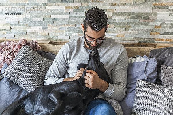 Mann kuschelt mit seinem Hund auf der Couch zu Hause