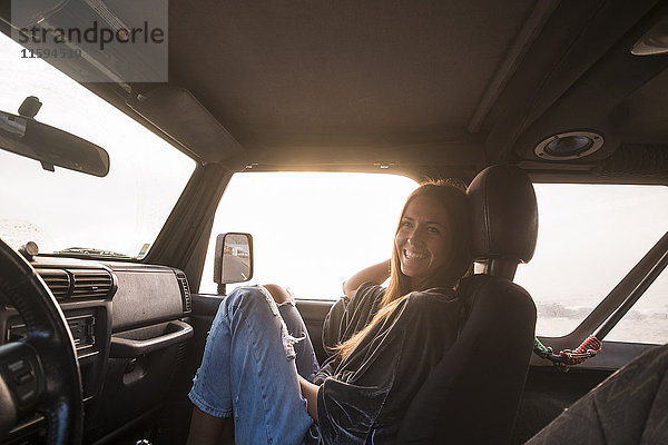 Lachende Frau bei Sonnenuntergang im Auto sitzend