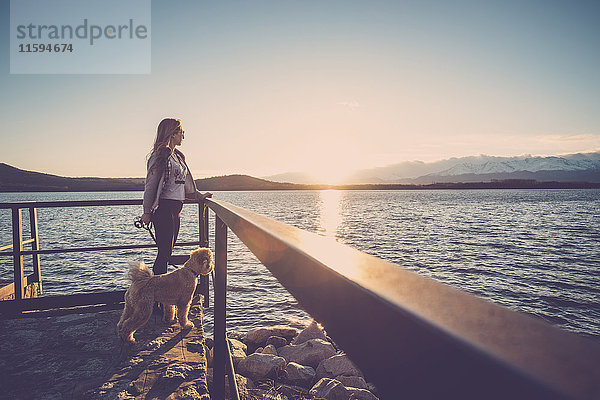 Frau am See bei Sonnenuntergang mit ihrem Hund