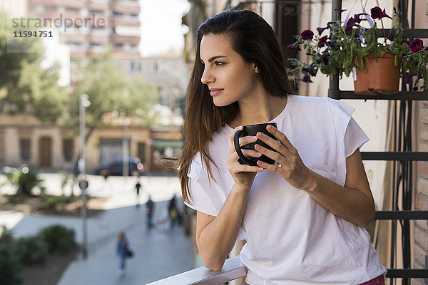Frau mit Kaffeetasse auf dem Balkon stehend mit Blick in die Ferne