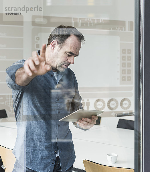 Geschäftsmann mit Tablett berührender Glasscheibe mit Daten im Büro
