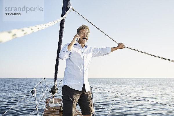 Lachender reifer Mann am Telefon auf seinem Segelboot