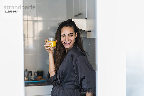 Porträt einer lachenden jungen Frau mit einem Glas Orangensaft in der Küche
