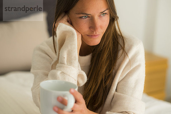 Junge Frau auf dem Bett sitzend mit einer Tasse Kaffee
