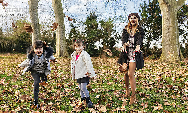 Mutter wirft Blätter mit ihren Töchtern im Herbstpark