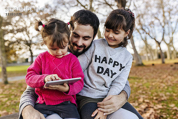 Vater mit seinen kleinen Töchtern beim Betrachten der Tafel im herbstlichen Park