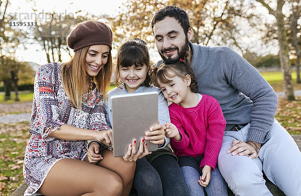 Familie sitzt auf einer Bank im herbstlichen Park und nimmt Selfie mit Tablette.