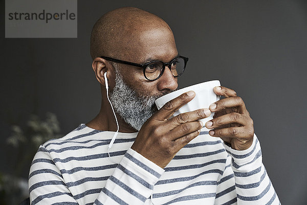 Erwachsener Mann mit Kopfhörern beim Kaffeetrinken