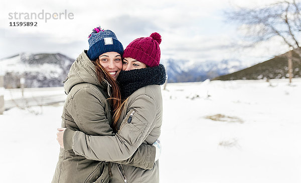 Zwei junge Frauen  die sich im Schnee umarmen.