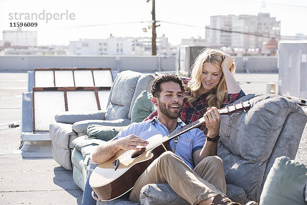 Paar auf rooptop sitzend auf Sofa und Gitarre spielend