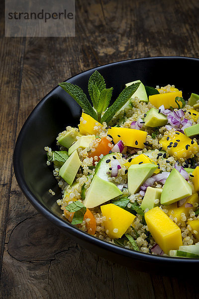 Schale mit Quinoa-Salat mit Mango  Avocado  Tomaten  Gurken  Kräutern und schwarzem Sesam