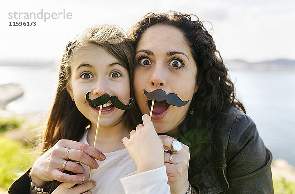 Mutter und Tochter haben Spaß daran  einen falschen Schnurrbart zu halten.