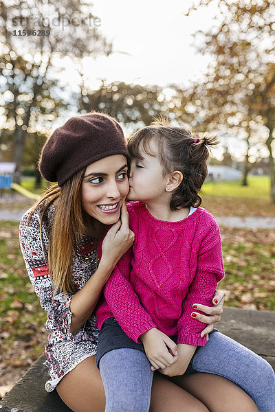 Kleines Mädchen  das seine Mutter im Herbstpark küsst.