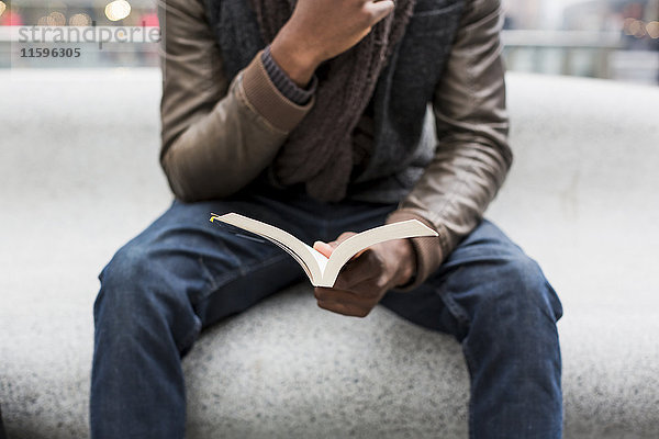 Junger Mann sitzt auf der Bank und liest ein Buch  Teilansicht