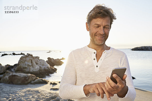 Porträt eines lächelnden Mannes mit Handy am Strand