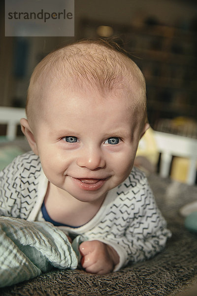 Fröhliches drei Monate altes Baby schaut auf und lächelt etwas in seiner Krippe an.