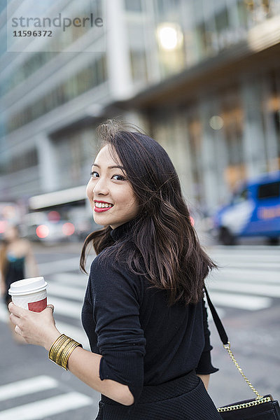 USA  New York City  Manhattan  Portrait einer lächelnden jungen Frau mit Kaffee zum Überqueren der Straße