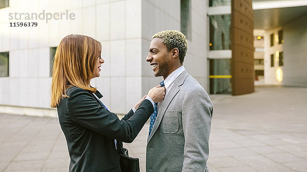 Junge Geschäftsfrau befestigt Krawatte des jungen Geschäftsmannes