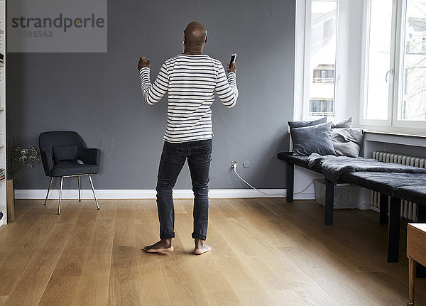 Ein reifer Mann  der alleine zu Hause tanzt und ein Smartphone hält.