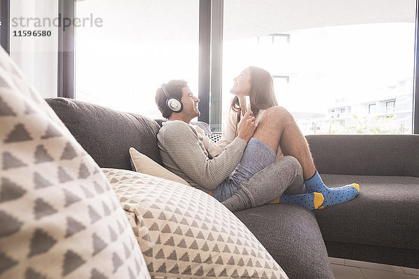 Glückliches junges Paar mit Kopfhörer und Smartphone auf der Couch