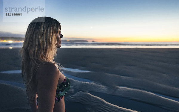 Junge Frau beobachtet den Sonnenuntergang am Strand