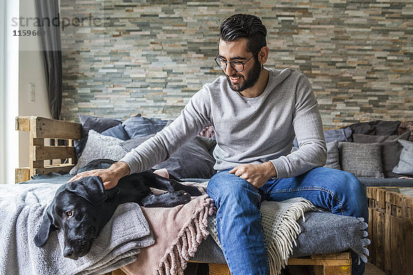 Mann  der seinen Hund zu Hause auf der Couch streichelt.