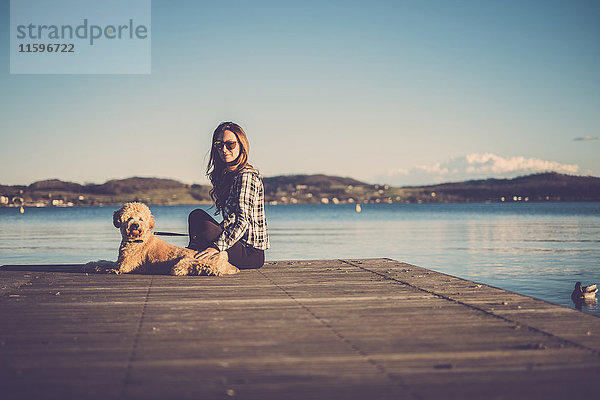 Frau sitzt mit ihrem Hund am Steg.