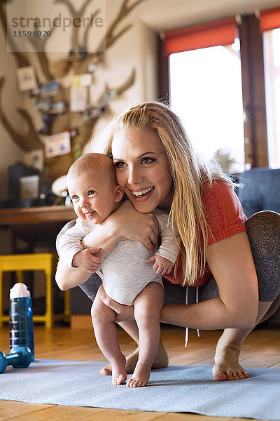 Lächelnde Mutter mit Baby und Fitnessgeräten zu Hause