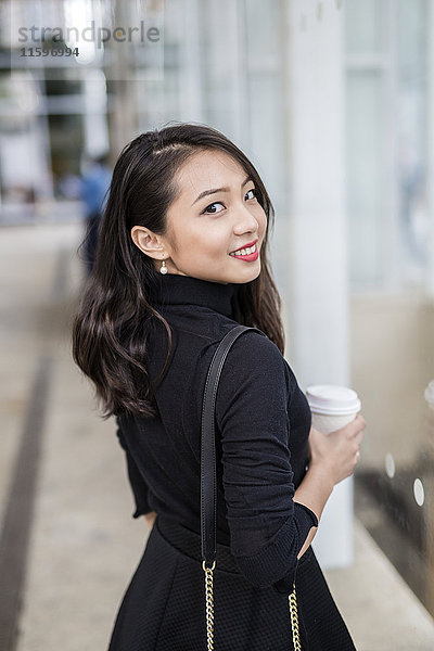 Porträt einer lächelnden jungen Frau mit Kaffee zum Über die Schulter schauen