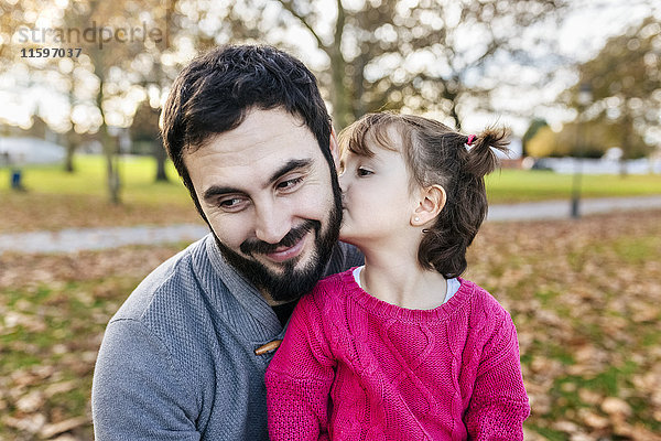 Kleines Mädchen  das seinen glücklichen Vater im Herbstpark küsst.