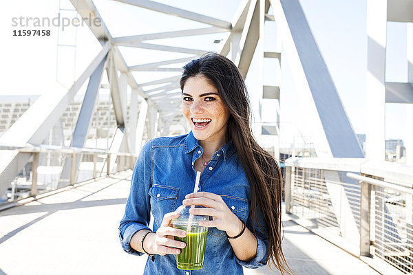 Spanien  Barcelona  Porträt der lächelnden jungen Frau mit Getränk auf einer Brücke