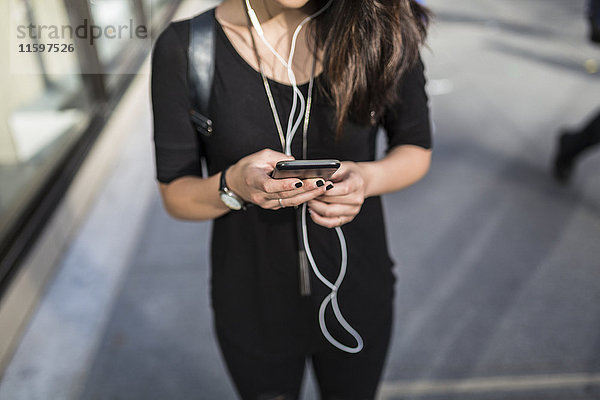 Junge Frau beim Musikhören mit Kopfhörern beim SMS-Versand  Teilansicht